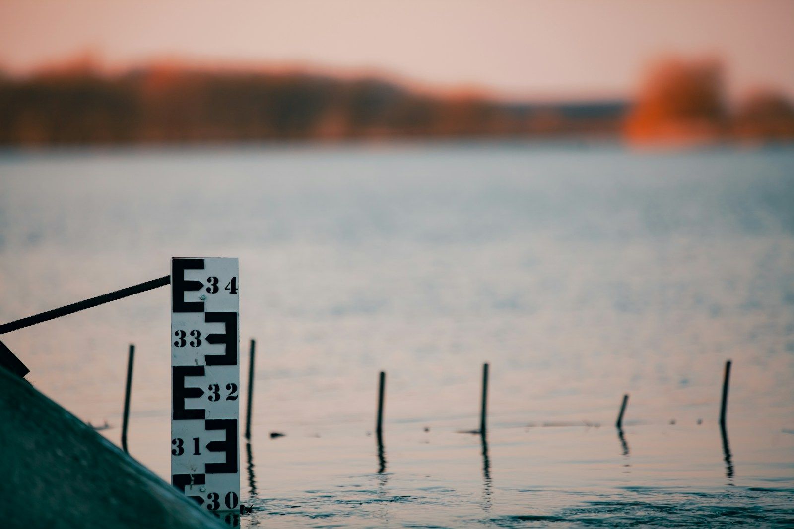 A numbered staff gauge standing in calm open water at dusk
