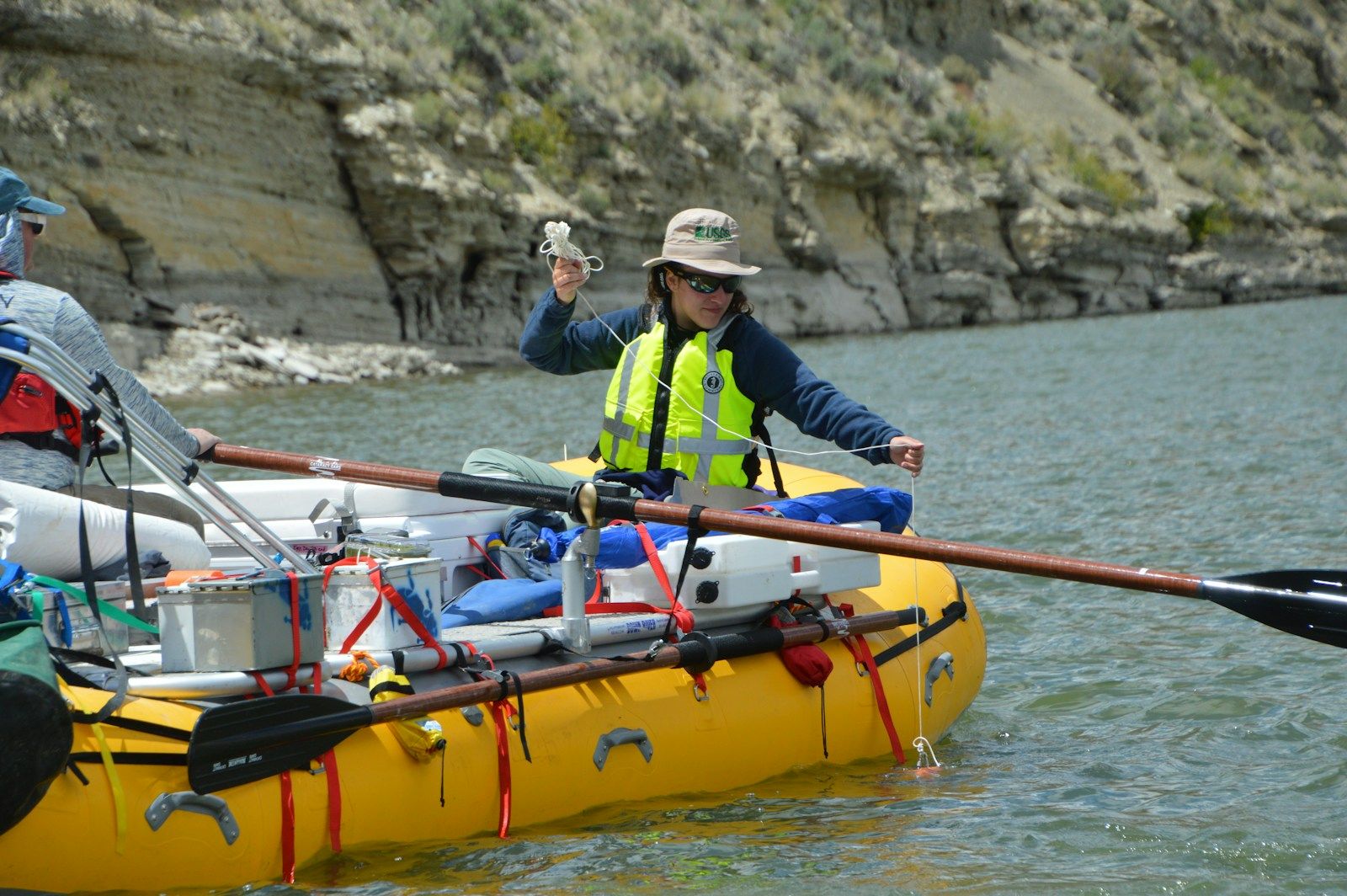 A person in a raft sampling water quality against a rock face